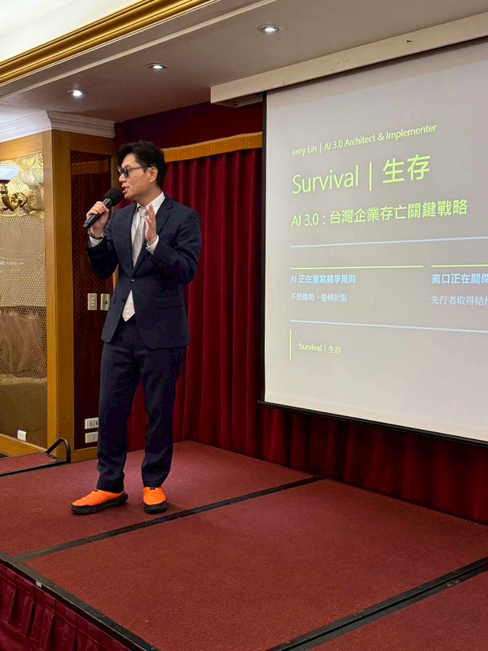 AIとビジネスについてのスライドの横で、マイクを手に話すJerry Lin